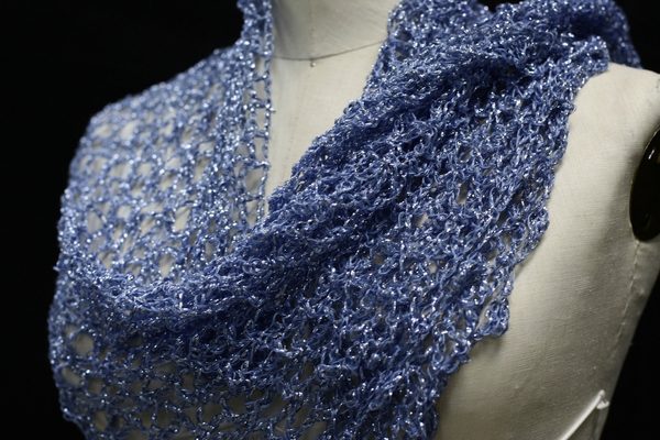 Blue lurex crochet shawl draped over a mannequin's shoulder, close side view of the shimmering openwork.