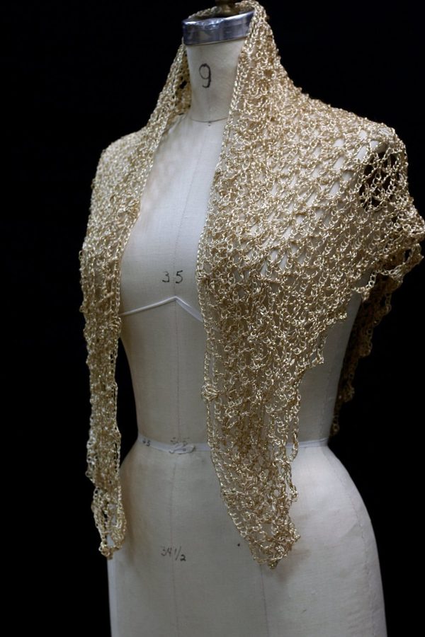 Gold beaded crochet shawl draped over a dress-form mannequin, front view of the shimmering wrap against a dark backdrop.