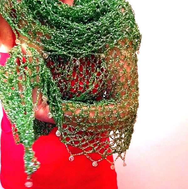 Woman in a red dress wearing a green lurex crochet shawl, the beaded edge with hanging beads draped over her arm.