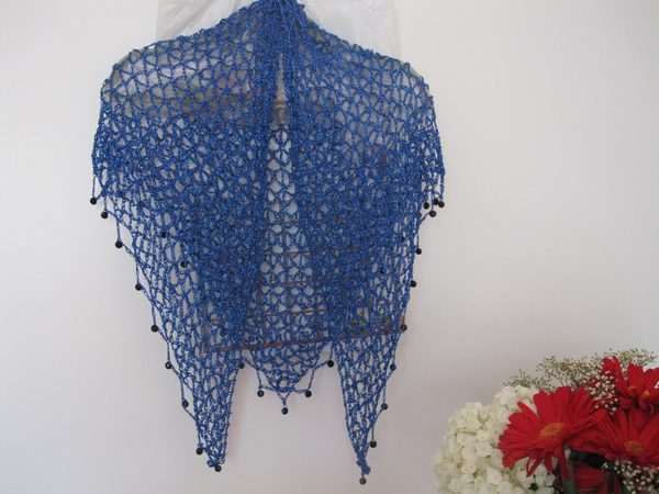 Sapphire blue lurex shawl hanging in a full drape, dark beads along the edge, flowers arranged below.